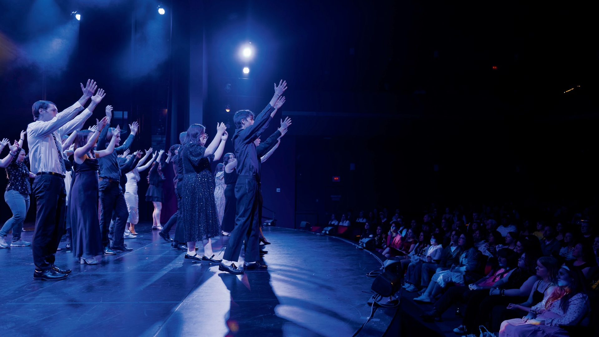 Cast with arms raised before an audience